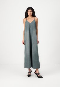 Denim maksikjole med tynne stropper, V-hals, løs passform og en lys blågrå farge. Kombinert med svarte hælsandaler med stropper og nagler.