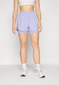 Unos pantalones cortos deportivos lila con cinturilla elástica y diseño en capas, hechos de una tela ligera; combinados con calcetines blancos y zapatillas.