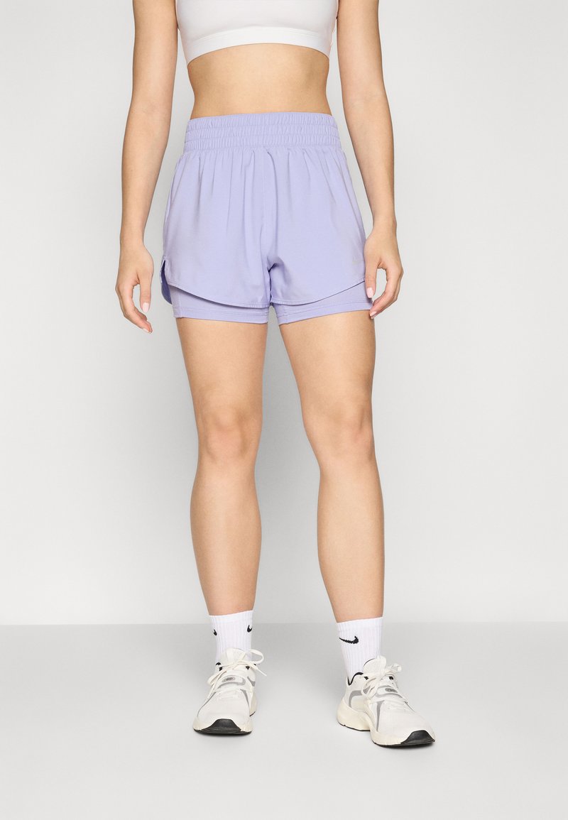 Unos pantalones cortos deportivos lila con cinturilla elástica y diseño en capas, hechos de una tela ligera; combinados con calcetines blancos y zapatillas.