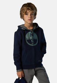 Felpa con zip color navy con dettagli grigi, dotata di un grande logo circolare sulla parte anteriore. Tasche frontali e tessuto morbido.