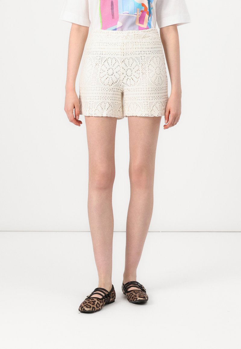 White crochet shorts with a scalloped hem, featuring floral patterns and a fitted waistband, paired with leopard print flats.