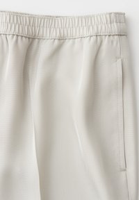 Pantaloni beige chiaro con vita elastica, tasca laterale sulla cucitura e trama a spina di pesce visibile nel tessuto.
