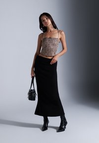 Cropped top met luipaardprint en dunne bandjes, gecombineerd met een zwarte rok tot de knie. Geaccessoireerd met een kleine zwarte handtas en haklaarzen.