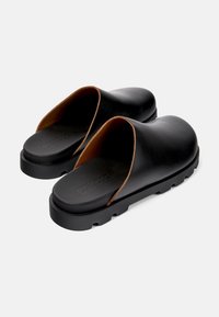 Sabots ouverts en cuir noir avec une finition lisse, des accents en cuir marron et une semelle en caoutchouc noir épaisse avec une texture antidérapante.