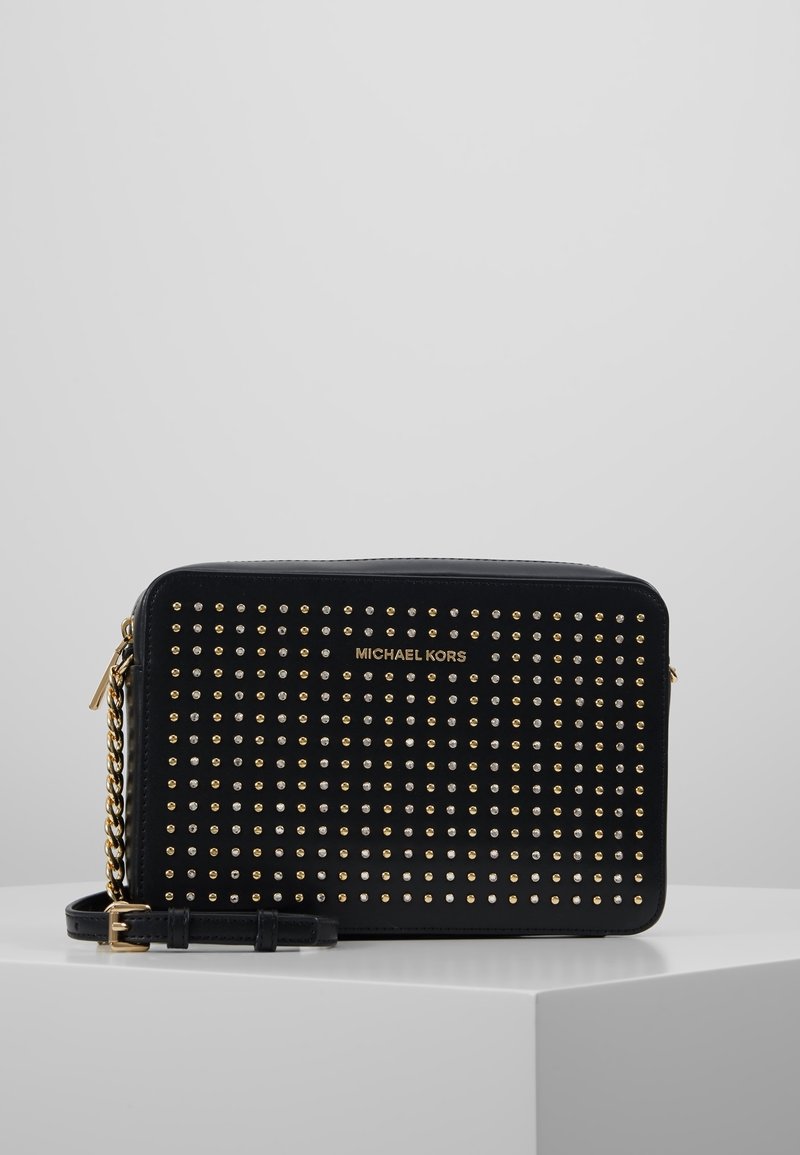 Borsa a tracolla nera rettangolare di Michael Kors con borchie dorate e argentate e una tracolla dorata, esposta su un piedistallo bianco.