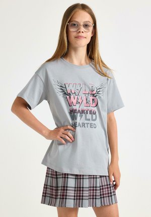 Grå bomull T-shirt med texten "WILD HEARTED" och vingar, kombinerad med en plisserad rutkjol i grått, vinrött och vitt.