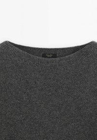 Pull en maille côtelée gris foncé avec col rond et une petite étiquette noire au dos du col.
