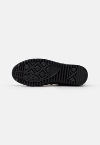 Suela de zapato de goma negra con un patrón de textura y tacos para tracción, con una zona de puntera lisa y un talón pronunciado para mayor estabilidad.