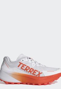 Hvid og orange trail løbesko med stort "TERREX" logo på siden og tekstureret sål for greb og komfort.
