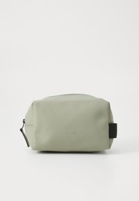 Green waterproof cosmetic bag with a smooth texture, rounded shape, black accent strap, and embossed "RAINS" logo on the front.