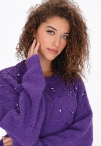 Paarse trui van zachte stof, versierd met decoratieve kralen in verschillende tinten paars en zilver over de voorkant en de mouwen.
