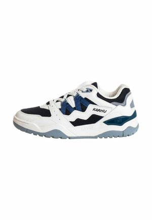 Scarpa sportiva bianca con accenti blu navy e grigio, realizzata in materiali in rete e pelle, suola testurizzata e lacci intrecciati in un design moderno e atletico.