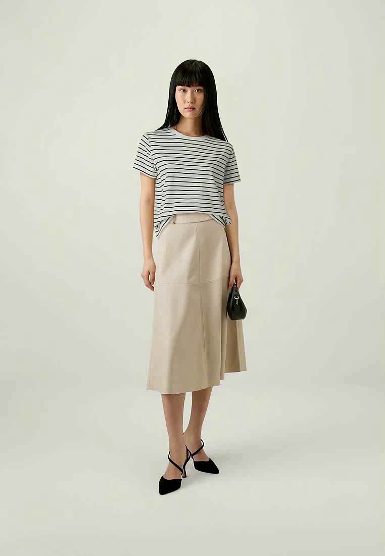 Femme portant un t-shirt rayé noir et blanc, une jupe midi beige, des escarpins noirs pointus et tenant un petit sac à main noir.