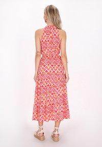 Rochie cu gât halter, cu un model în zigzag roz, portocalie și galben, cu un design în straturi și margine până la glezne, asociată cu sandale espadrile.