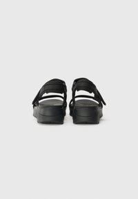 Black sandals featuring a simple design with adjustable straps, a textured sole, and a rounded shape for comfort.