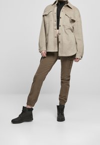 Béžová oversize flanelová bunda s kapsami na prsou, černý crop top, olivové cargo kalhoty s elastickými manžetami a černé kotníkové boty.