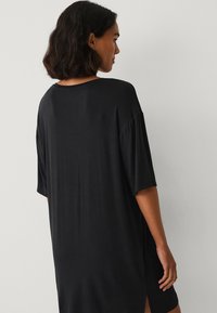 Sort oversized t-shirt kjole med korte ærmer, afslappet pasform, sideslids og glat tekstur. Bagpå har den en rund halsudskæring.