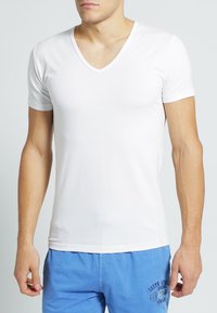 T-shirt bianco a maniche corte con scollatura a V, realizzato in un tessuto leggero e morbido. Presenta un design aderente e un’etichetta discreta in basso a sinistra.