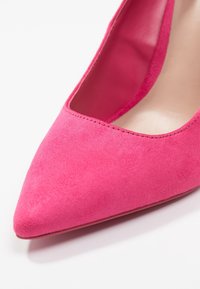 Chaussure à talon haut en daim rose avec un bout pointu. La tige a une texture lisse et l'intérieur est doté d'une doublure beige.