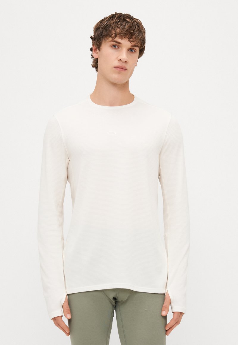Lahka dolga majica v off-white barvi, z okroglim izrezom in subtilno teksturo. Ožji kroj z logotipom na prsih.