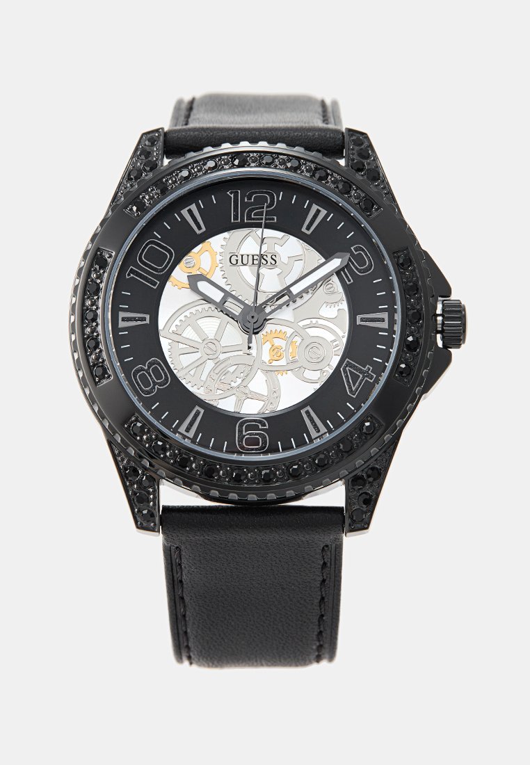 Reloj analógico negro con un dial de esqueleto transparente, números arábigos en negrita y una correa de cuero texturada con un bisel de metal adornado con acentos negros.