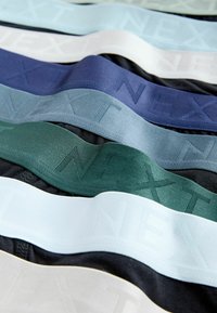 Texturált elasztikus derékpántok több színben: világoskék, fehér, zöld, tengerészkék és fekete, mindegyiken a „NEXT” márkanév dombornyomott logóval.