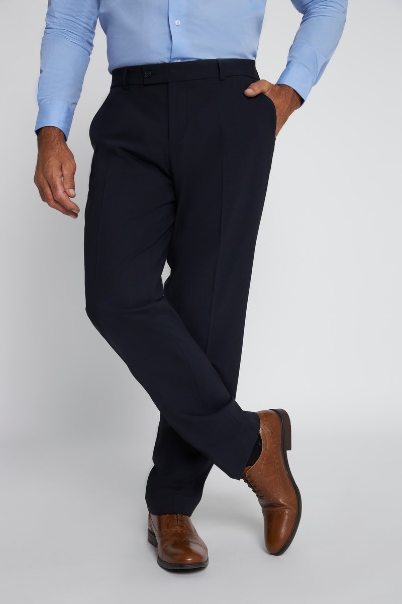 Man draagt zwarte nette broek, blauwe blouse met knopen en bruine leren nette schoenen, met één hand in de zak en benen gekruist.
