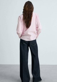 Camicia a righe rosa chiaro con bottoni e maniche lunghe, abbinata a pantaloni a gamba larga in denim scuro a vita alta. Texture morbide e design classico.