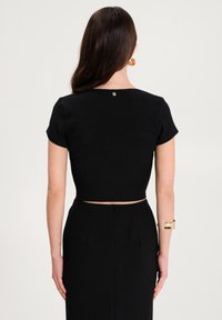 Czarny krótki top z krótkimi rękawami, żebrowana tekstura i mały złoty guzik z tyłu. Połączony z pasującą spódnicą o wysokim stanie.