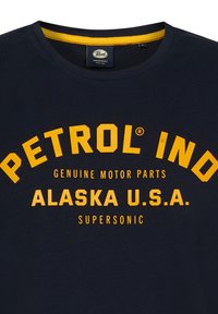 Námořnická modrá bavlněná tričko s výrazným žlutým textem: "PETROL IND AUTENTICKÉ MOTOROVÉ DÍLY ALJAŠKA USA SUPERSONIC." Kulatý výstřih.