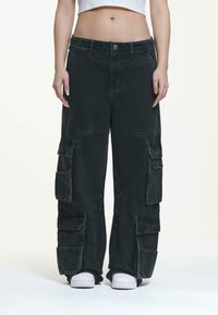 Black cargo pants with a loose fit, multiple pockets, and a slightly faded texture. Fastened with a button and featuring an elastic waistband.