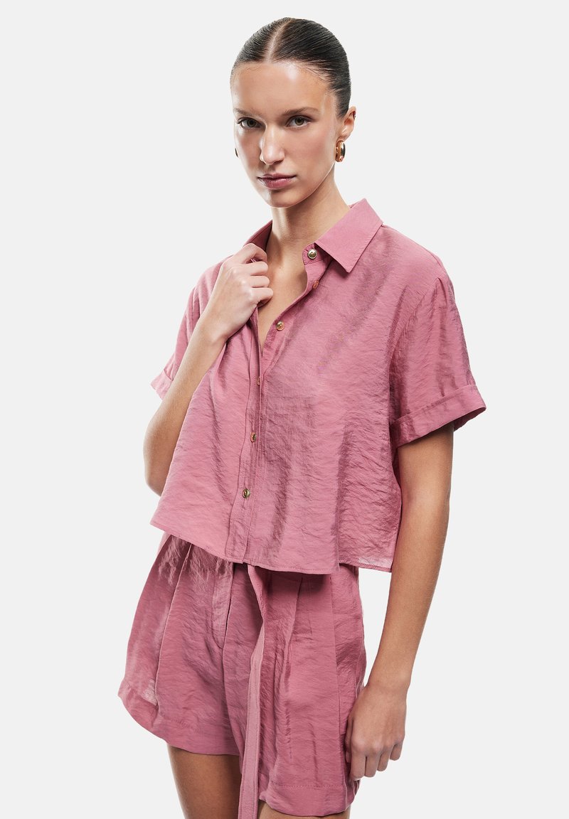 Rosa, taillierte Button-Up-Bluse mit kurzen Ärmeln und strukturiertem Stoff, kombiniert mit passenden Shorts. Verfügt über goldfarbene Knopfdetails.