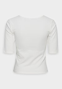 Bílá žebrovaná košile s krátkým rukávem a kulatým výstřihem z pohledu zezadu na jednoduchém bílém pozadí.