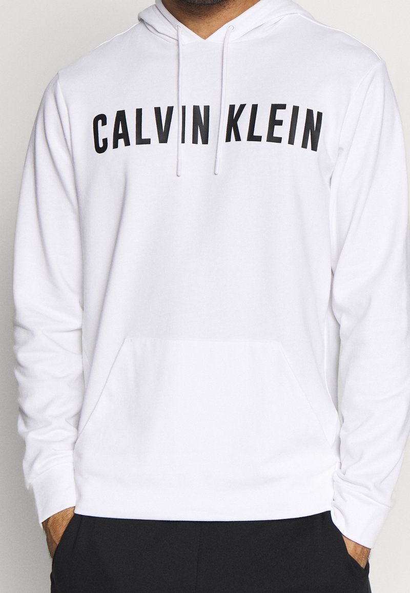 Sweat à capuche blanc en mélange de coton, avec une poche avant et un texte noir audacieux "CALVIN KLEIN" sur la poitrine.