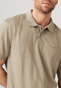 Khaki polo shirt laget av bomull, med klassisk krage, to-knapps åpning og brodert logo på brystet. Glatt tekstur.