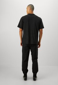 Sort bomulds T-shirt med afslappet pasform, korte ærmer og rund hals, sammen med matchende sorte bukser og athletic sko.