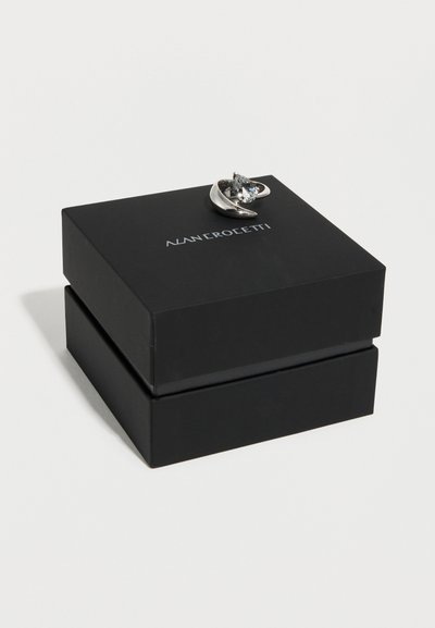 Ασημένιο δαχτυλίδι με μεγάλο τριγωνικό διαυγές πολύτιμο λίθο πάνω σε μαύρο κουτί με την ετικέτα "Alan Crocetti" σε απλό λευκό φόντο.