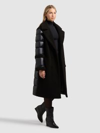 Fekete kabát, dudoros ujjú kialakítással, texturált gyapjútesttel, dupla soros gombolással és térd hosszúságú szabással. Stílusos fekete csizmával viselve.