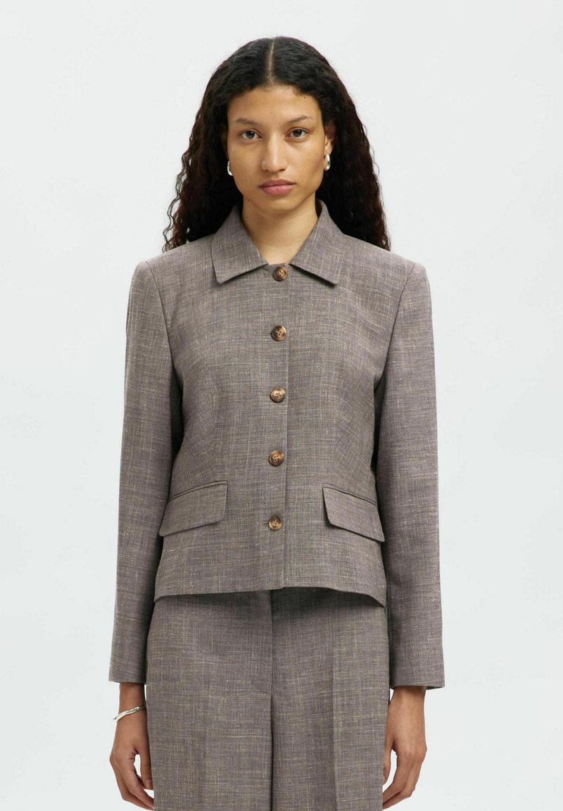 Blazer aderente in tweed marrone con colletto, chiusura a bottoni e due tasche frontali. Presenta un tessuto testurizzato e bottoni in legno naturale.