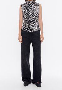 Top senza maniche bianco e nero con design a stampa zebra, abbinato a jeans neri a gamba larga. Tessuto liscio con collo alto.