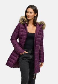 Fialová zateplená bunda s kožušinovou kapucňou, prešívaný dizajn, zips a bočné vrecká, nosená cez čierne tričko a tmavé džínsy.
