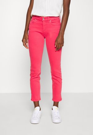 Jeans de mezclilla rosa con un corte ajustado, que cuentan con un diseño clásico de cinco bolsillos, cierre de botón y puños enrollados. Combinados con zapatillas blancas.