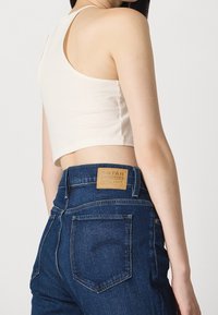 Světle béžový zkrácený top spárovaný s tmavě modrými džíny s vysokým pasem, které mají koženou etiketu a viditelné zadní kapsy.