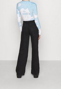 Blusa de manga larga con un patrón de nubes en azul y blanco, combinada con pantalones de pierna ancha negros de cintura alta. La tela parece suave con un ligero brillo.