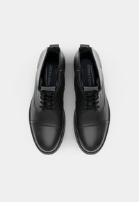 Botas de ankle de cuero negro con un acabado suave, diseño de cordones y cremallera, con sutiles detalles de costura y una forma de punta redondeada.