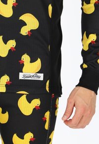 Black long-sleeve top with a ribbed texture, featuring yellow rubber duck patterns. Includes a prominent brand tag near the hem.