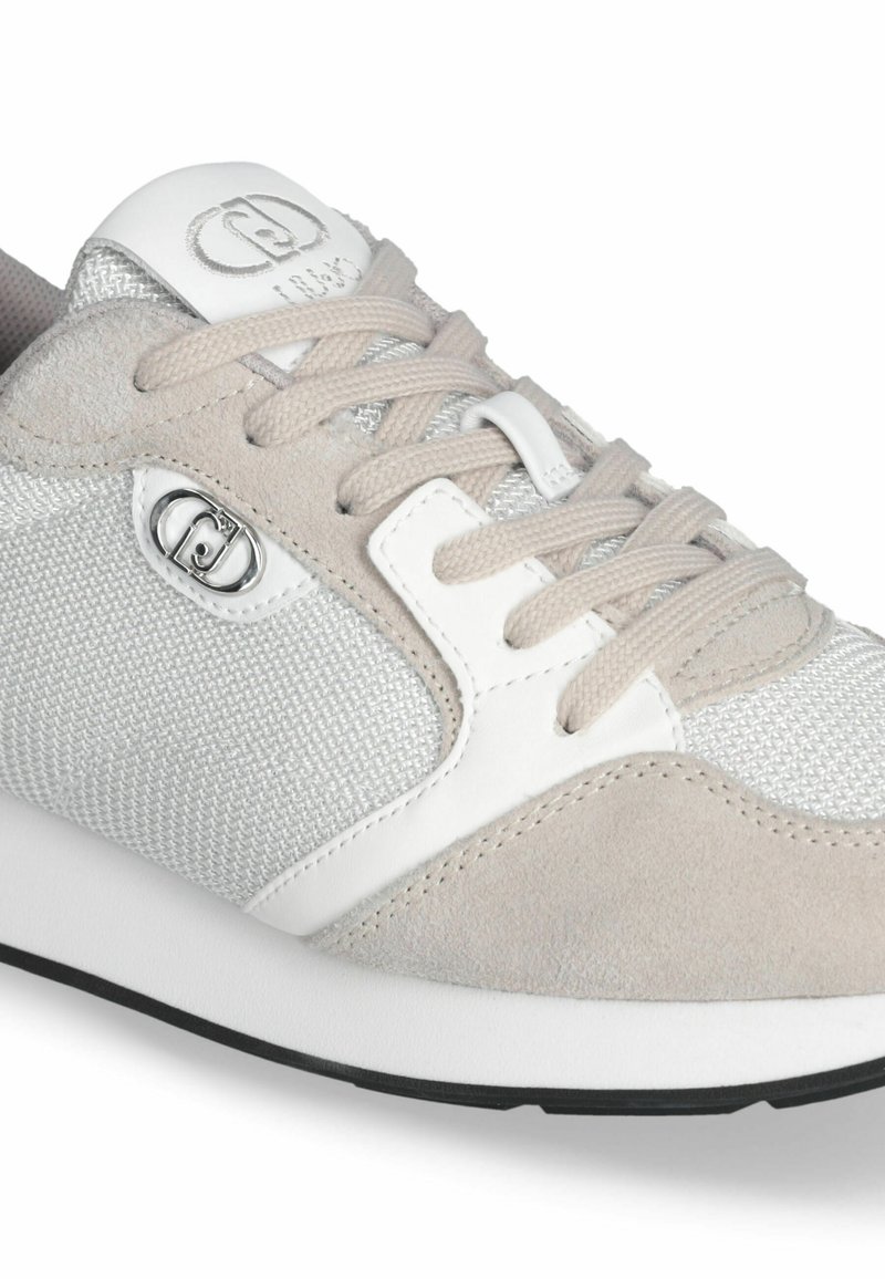 Chaussure de sport gris clair en mesh et suède. Comprend des accents argentés et un logo blanc sur la languette, avec des lacets plats et une semelle en caoutchouc.