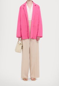 Veste rose oversized, haut crème avec détails en dentelle, pantalon large beige et sac à main beige. Texture lisse, ferrures minimalistes et couleurs vives.