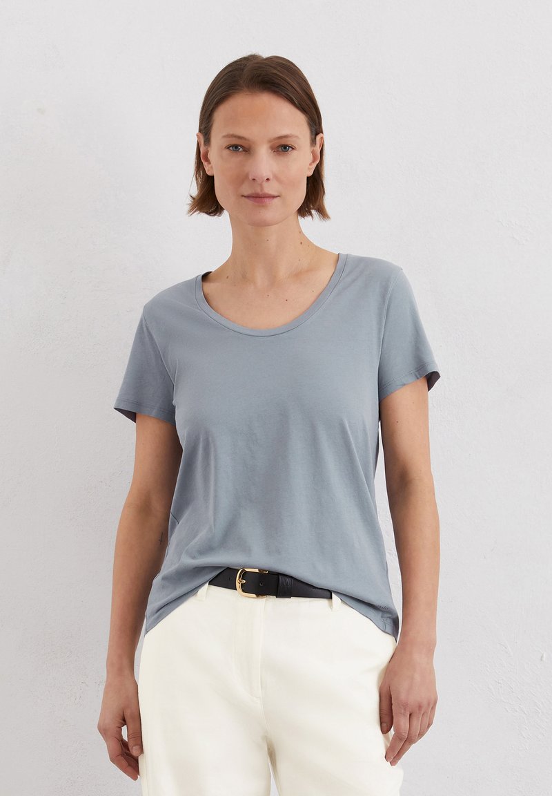 Lichtblauw T-shirt met korte mouwen en een ronde hals. Gemaakt van zachte stof, heeft het een relaxte pasvorm en een gladde textuur, gecombineerd met witte broeken.