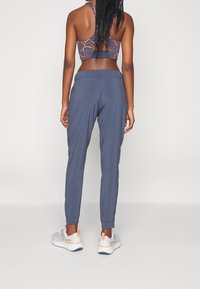 Gray athletic pants made of lightweight fabric, featuring a tapered leg design and elastic waistband, paired with gray and white running shoes.